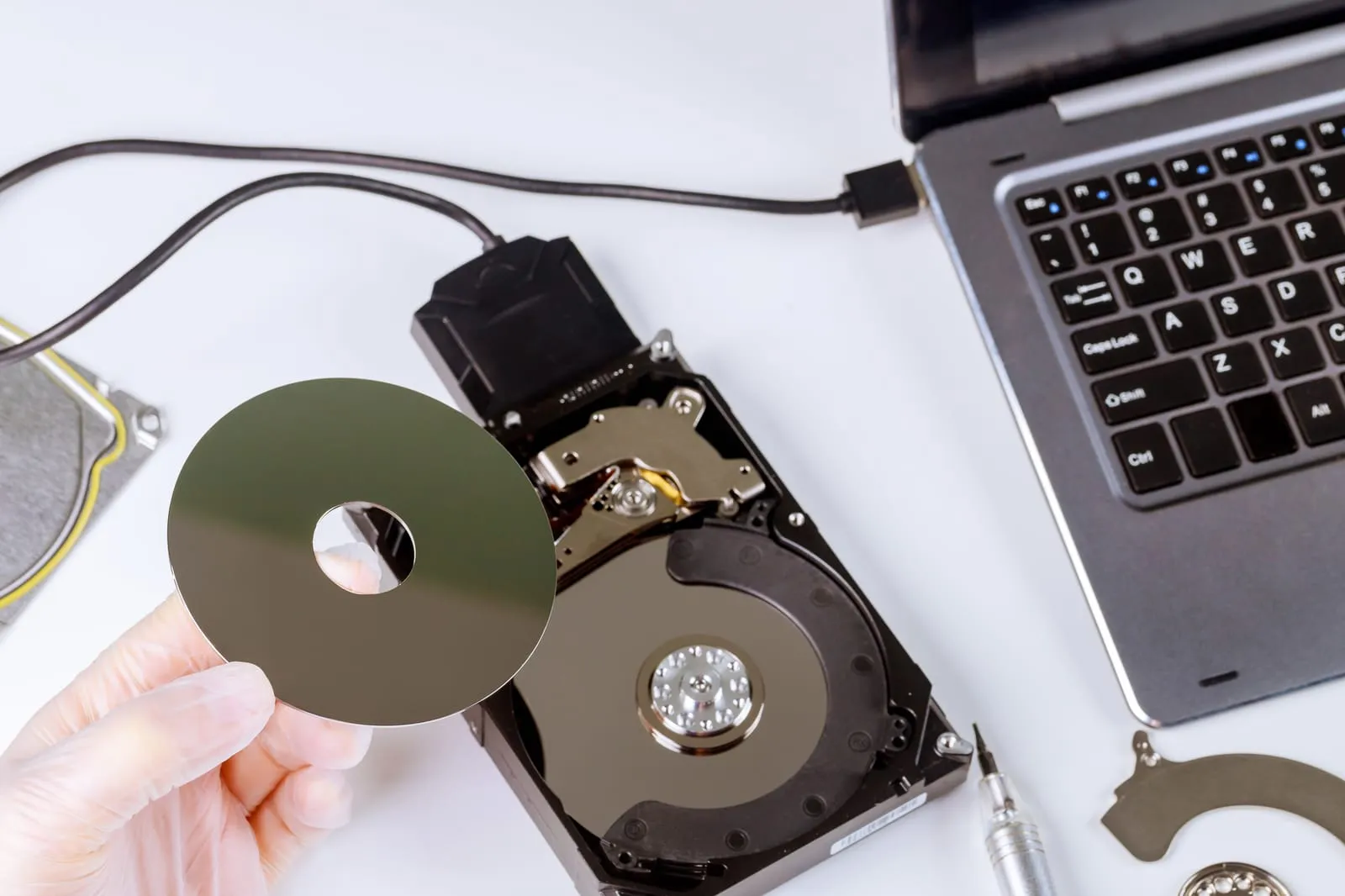 A hard drive opened on the bench to recover its data, connected to a laptop